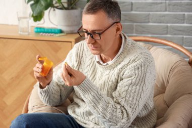 Orta yaşlı bir adam evde hap şişesinden hap alıyor.