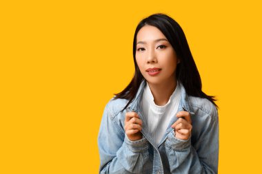 Sarı arka planda şık kot ceketli güzel bir Asyalı kadın.