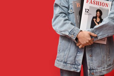 Kırmızı arka planda dergisi olan şık kot elbiseli güzel bir Asyalı kadın.