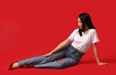 Kırmızı arka planda oturan şık kotlu güzel Asyalı kadın.