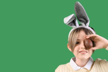 Yeşil arka planda çikolatalı yumurtası olan tavşan kulaklı şirin bir çocuk. Paskalya kutlaması