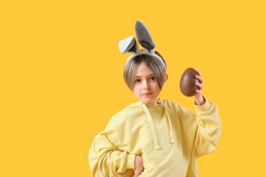 Sarı arka planda çikolata yumurtası olan tavşan kulaklı şirin bir çocuk. Paskalya kutlaması