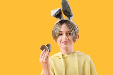 Sarı arka planda yarım çikolatalı yumurtası olan tavşan kulaklı şirin bir çocuk. Paskalya kutlaması