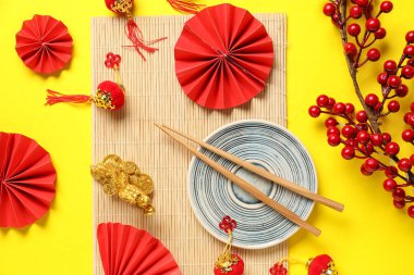 Bamboo mat with plate, chopsticks and decor on yellow background. Chinese table setting