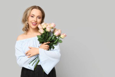 Gri arka planda güzel güllerle dolu buketi olan mutlu genç bir kadın.