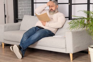 Oturma odasında kitap okuyan üzgün yaşlı adamın portresi.