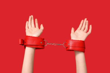 Kırmızı arka planda seks dükkanından kelepçeli kadın elleri.