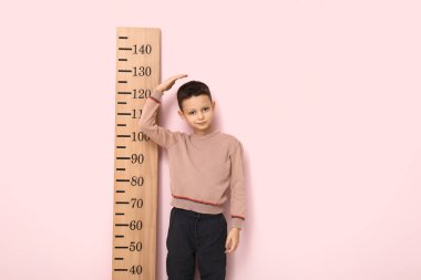 Pembe arka planda boyunu ölçen sevimli küçük bir çocuk.