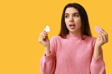 Sarı arka planda pembe kağıt kalplerle şok olmuş genç bir kız. Sevgililer Günü kutlaması