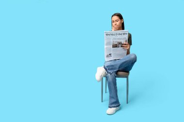 Mavi arka planda gazetesi olan düşünceli genç bir kadın.