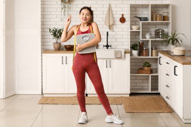Spor giyimli genç bir kadın, ağırlık tartısı ve mezura ile evde şans diliyor. Zayıflama konsepti