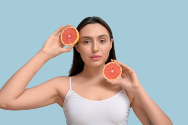 Mavi arka planda taze greyfurt olan güzel genç bir kadın.