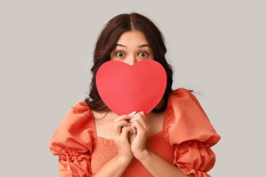 Gri arka planda kırmızı kağıt kalpli güzel bir Asyalı kadın. Sevgililer Günü kutlaması