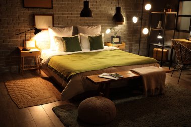 Şık bir yatak odası, yeşil bir battaniye ve geceleri parlayan lambalar.