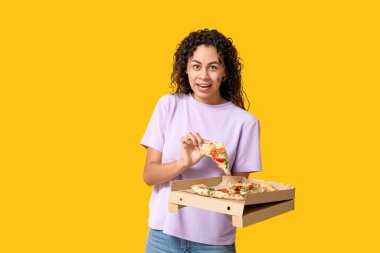 Sarı arka planda lezzetli pizzası olan güzel, mutlu, Afro-Amerikalı bir kadın.