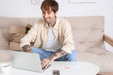 Evde online alışveriş yapan, hediye kartı ve dizüstü bilgisayarı olan dövmeli bir genç.