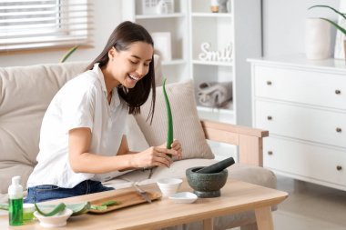 Güzel, genç, mutlu bir kadın oturma odasında aloe vera jeli yapıyor.