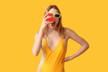 Tank mayo giyen ve sarı arka planda kokteyl içen güzel bir kadın.