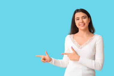 Genç, mutlu, gülümseyen kadın mavi arka plandaki bir şeyi işaret ediyor.