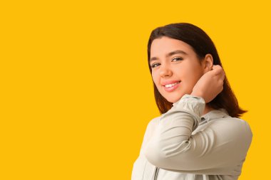 Sarı arka planda eli yüzüne yakın gülümseyen genç bir kadın.