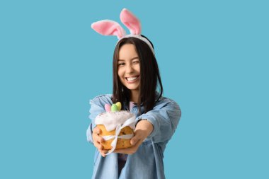 Tavşan kulaklı güzel bir genç kadın ve mavi arka planda Paskalya pastası.