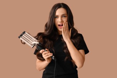 Bej arka planda saç maşası olan şaşırmış genç bir kadın.