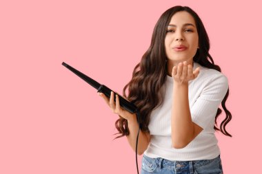 Pembe arka planda saç maşasıyla öpüşen güzel genç bir kadın.