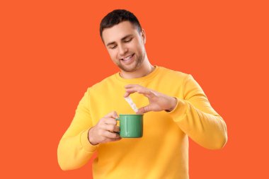 Turuncu arka planda çay ve şeker küpleri olan genç bir adam.