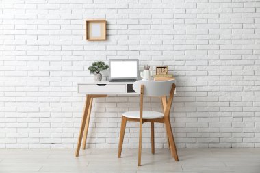 Beyaz duvarın yanında dizüstü bilgisayarı ve sandalyesi olan şık bir iş yeri.
