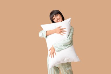 Kahverengi arka planda yumuşak yastıklı pijamalı güzel bir kadın.