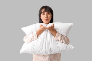 Gri arka planda yumuşak yastıklı pijamalı güzel bir genç kadın öpüşüyor.