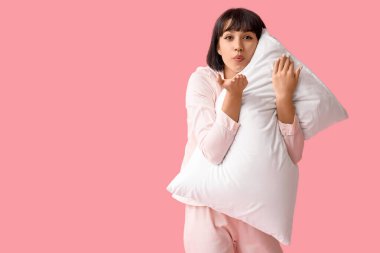 Pijamalı, yumuşak yastıklı, pembe arka planda öpüşen güzel bir kadın.