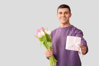 Beyaz arka planda hediye kutusu ve laleleri olan yakışıklı bir adam.
