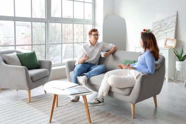 Genç çift oturma odasındaki gri koltukta sohbet ediyor.
