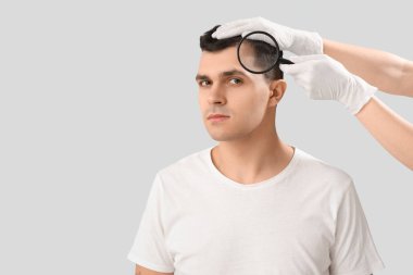 Büyüteçle doktor genç adamın saçlarını tarıyor. Arka planda, yakın plan.