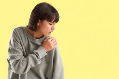 Sarı arka planda omuz ağrısı çeken genç bir kadın.