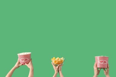 Yeşil arka planda patlamış mısır ve patates cipsi dolu kovaları tutan eller.