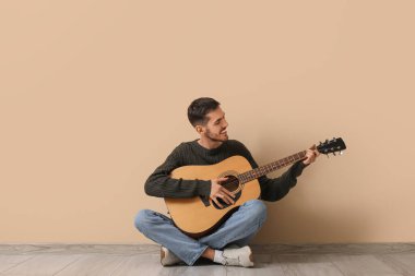 Bej arka planda gitar çalan yakışıklı genç adam.