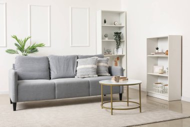 Gri kanepe, masa ve raf üniteleriyle aydınlık oturma odasının içinde.