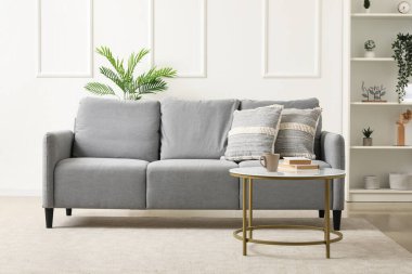 Gri kanepe, masa ve raf ünitesiyle aydınlık oturma odasının içinde.