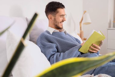 Genç adam yatak odasında kitap okuyor.