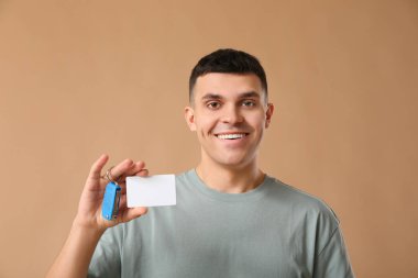 Boş ehliyeti ve kahverengi arka planda araba anahtarı olan mutlu genç adam.
