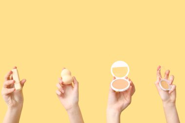 Sarı arka planda sünger, ruj ve pudra olan kadın elleri.