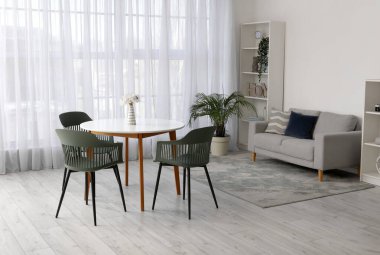 Masası, sandalyeleri, kanepesi, çiçekleri ve raf ünitesi olan modern oturma odasının içinde.