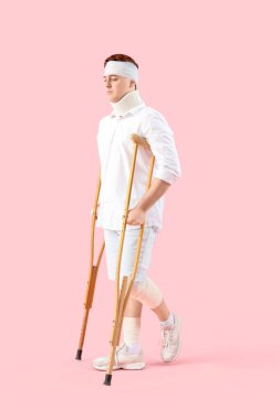 Pembe arka planda yürüyen koltuk değnekleriyle kazadan sonra yaralanan genç adam.