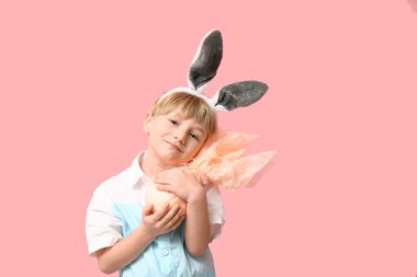 Pembe arka planda Paskalya hediyesi yumurtası olan tavşan kulaklı şirin bir çocuk.