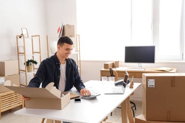 Depodaki masada hesap makinesiyle çalışan bir erkek çevrimiçi mağaza satıcısı