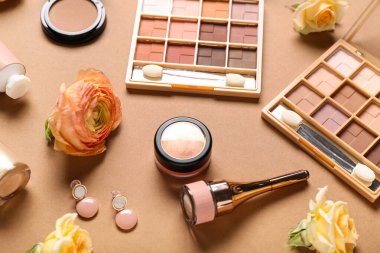 Kahverengi arka planda küpeli ve güllü makyaj ürünleri
