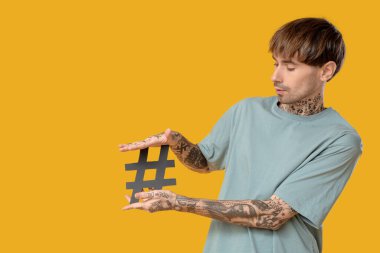 Sarı arka planda etiket sembolü olan havalı dövmeli genç adam.