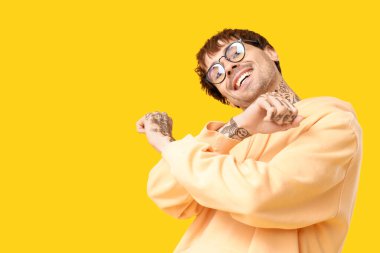 Sarı arka planda dans eden dövmeli genç adam.